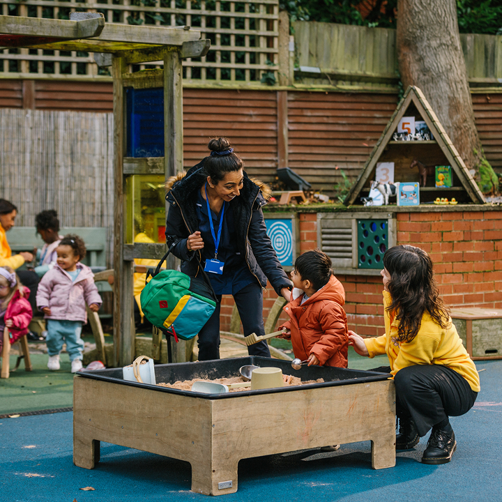 Children playing outside with sandpit at nursery at pick up time (mother figure picking little boy up)
