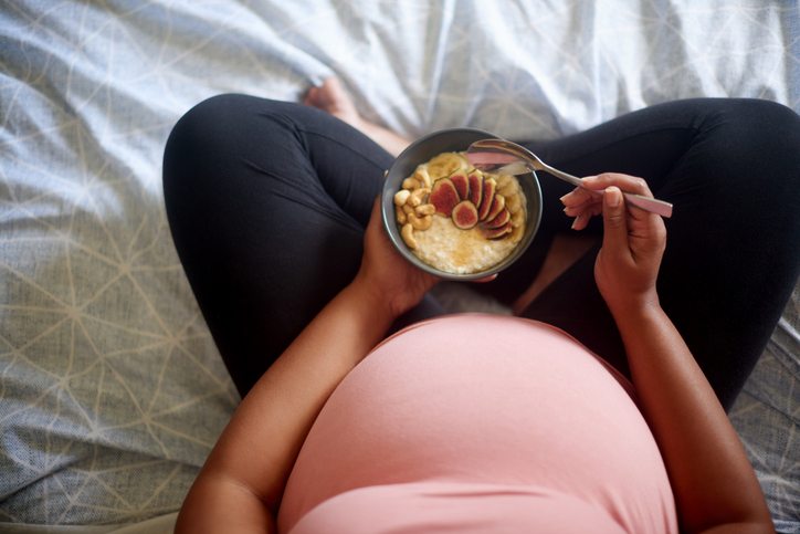 Pregnant woman eating a bowl of porridge topped with fruit