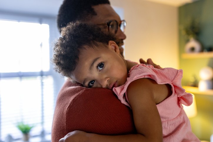 Young child resting their head on a parent's shoulder