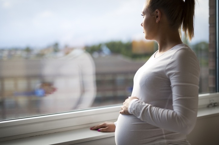 Pregnant woman standing by a window looking outside