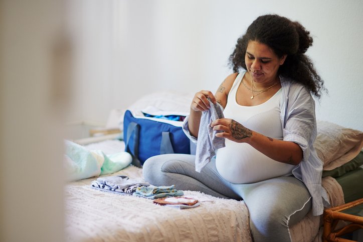 Pregnant woman packing baby clothes into a hospital bag