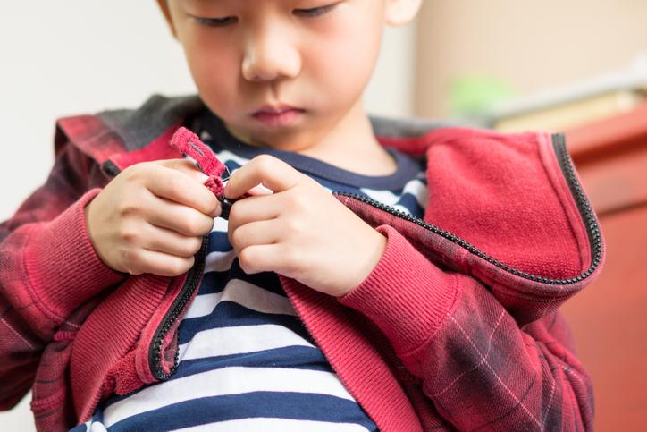 Pre-school boy attempting to zip up his hoodie.