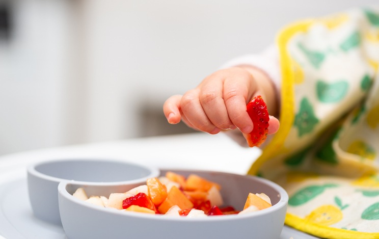 Baby picking up a strawberry from a bowl of chopped fruit