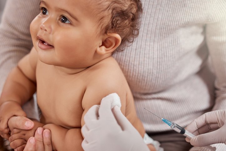Baby being held while a healthcare professional prepares to give a vaccination