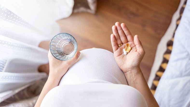 Pregnant woman holding a glass of water and vitamin tablets
